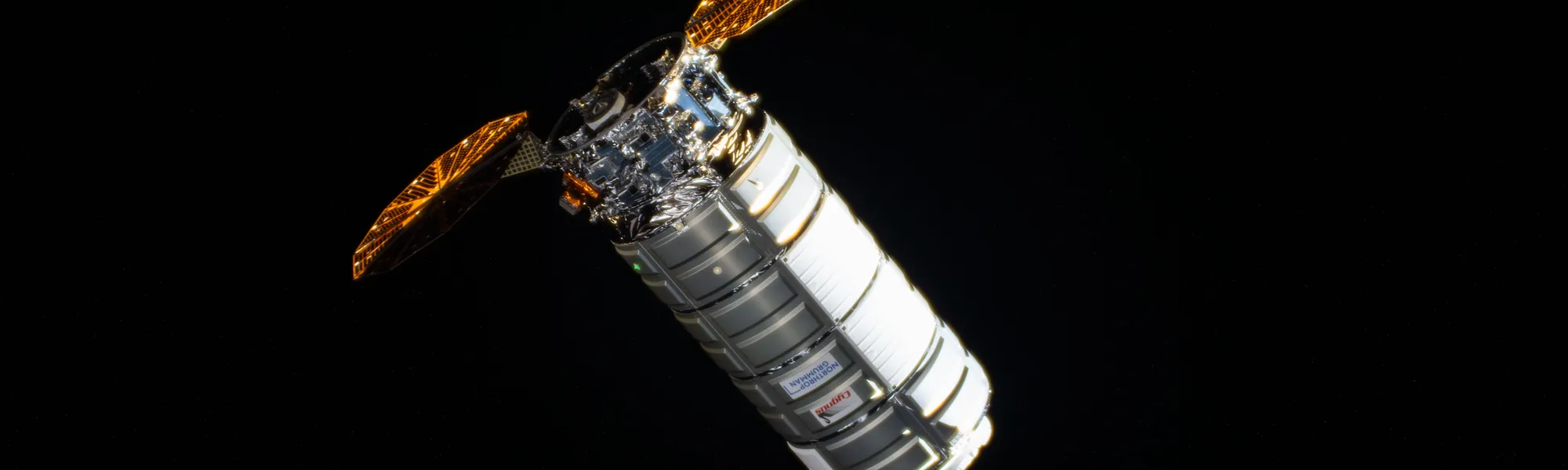 Northrop Grumman's Cygnus XL cargo spacecraft against black space, orange solar arrays deployed, on final approach to the International Space Station.